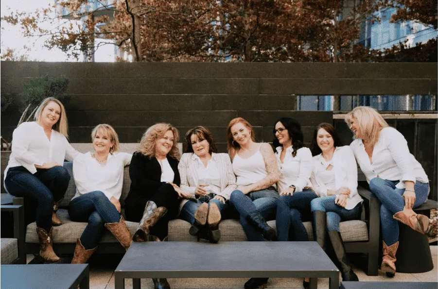 Team group photo outdoors with Kathleen Mason-Morton, PA-C in casual white tops – Med Spa Edmond OK Kathleen Mason-Morton, PA-C and the team in white shirts and jeans sitting together on an outdoor sofa, representing a friendly and professional med spa staff – Med Spa Edmond OK